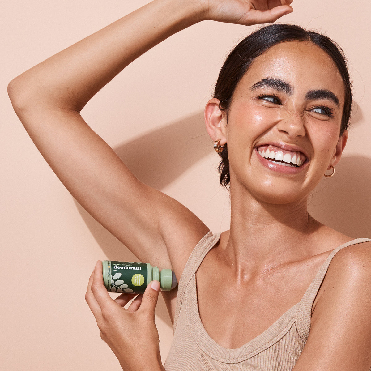 Smiling woman applying a bottle of A bit Hippy Bergamont on a peach background, natural aluminium free deodorant. 