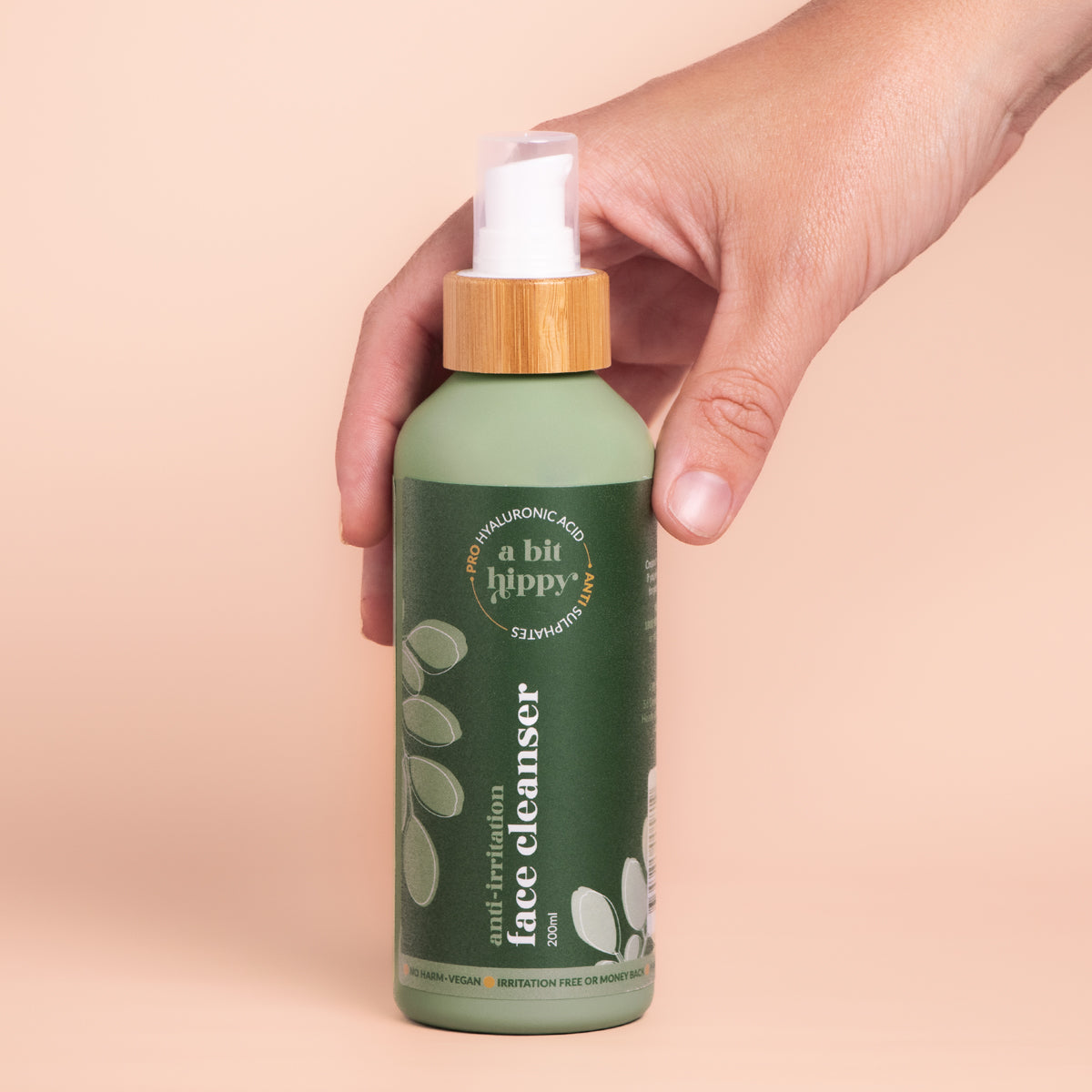 Hand holding A bit Hippy Face Cleanser 200ml bottle on peach background, Sulphate and SLS free cleanser with Hyaluronic Acid and Ceramides.