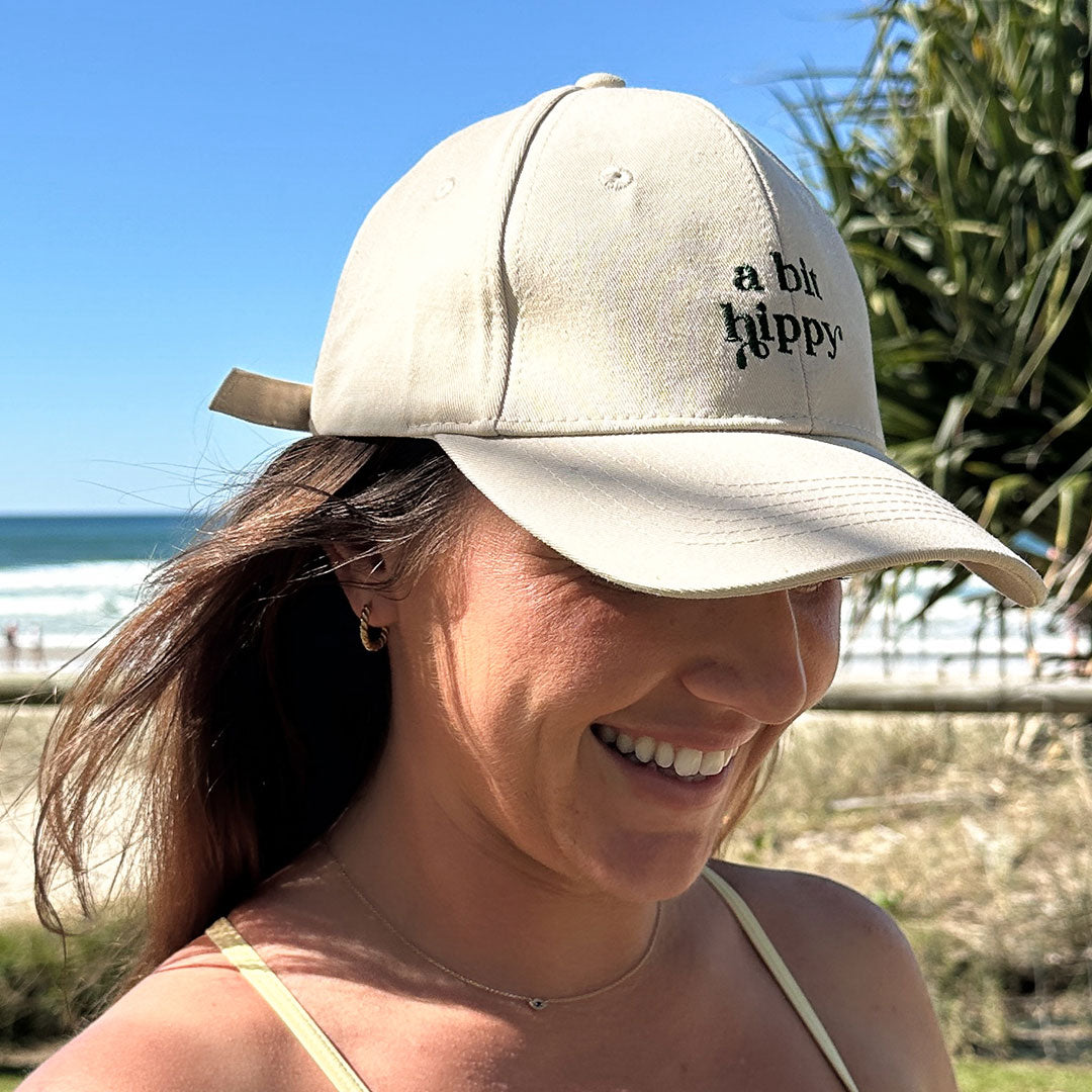 A Bit Hippy Cap worn at beach, lightweight beige cotton hat providing scalp and face sun protection, casual eco style for summer outdoor wear.