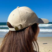 A Bit Hippy Cap worn at beach, lightweight beige cotton hat providing scalp and face sun protection, casual eco style for summer outdoor wear.