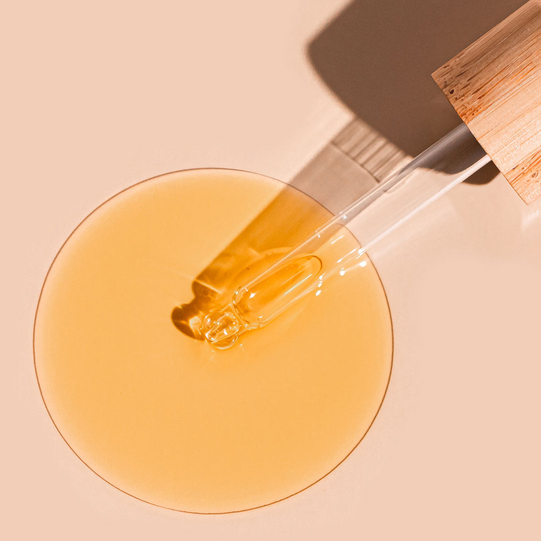 A bit Hippy Face Oil swatch on peach background, golden oil with Vitamin C and E along with Rosehip to improve skin elasticity and promote regeneration.