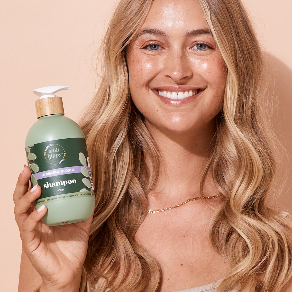 Blonde woman with healthy hair holding A bit Hippy shampoo bottle, designed to hydrate, brighten and smooth blonde hair