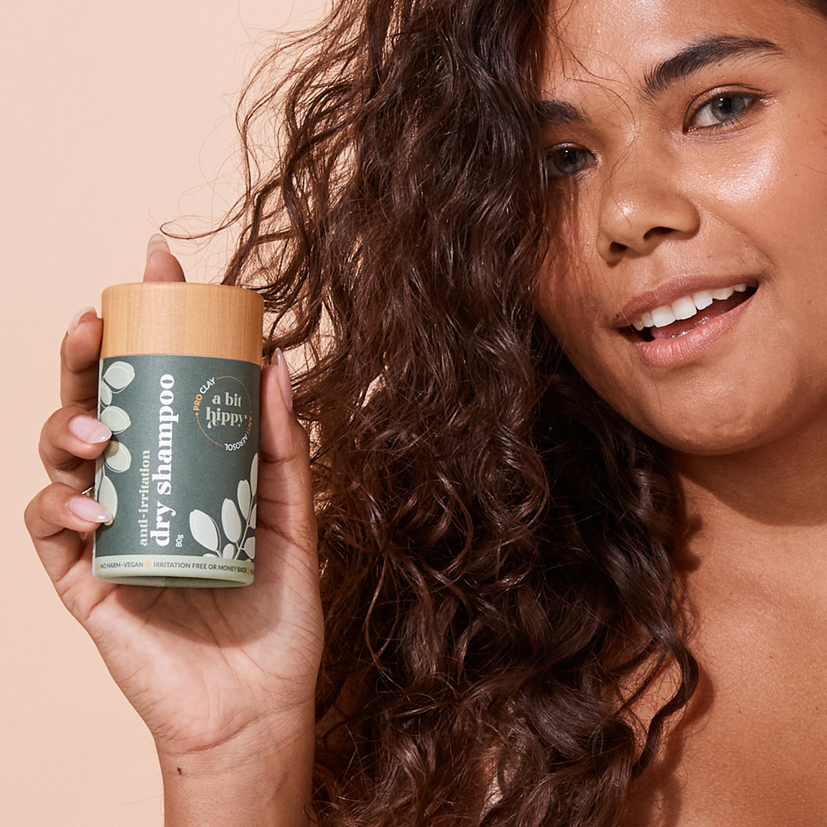 Woman holding 80g green A bit Hippy anti-irritation dry shampoo container on peach background, irritation and alcohol free hair washing alternative. 