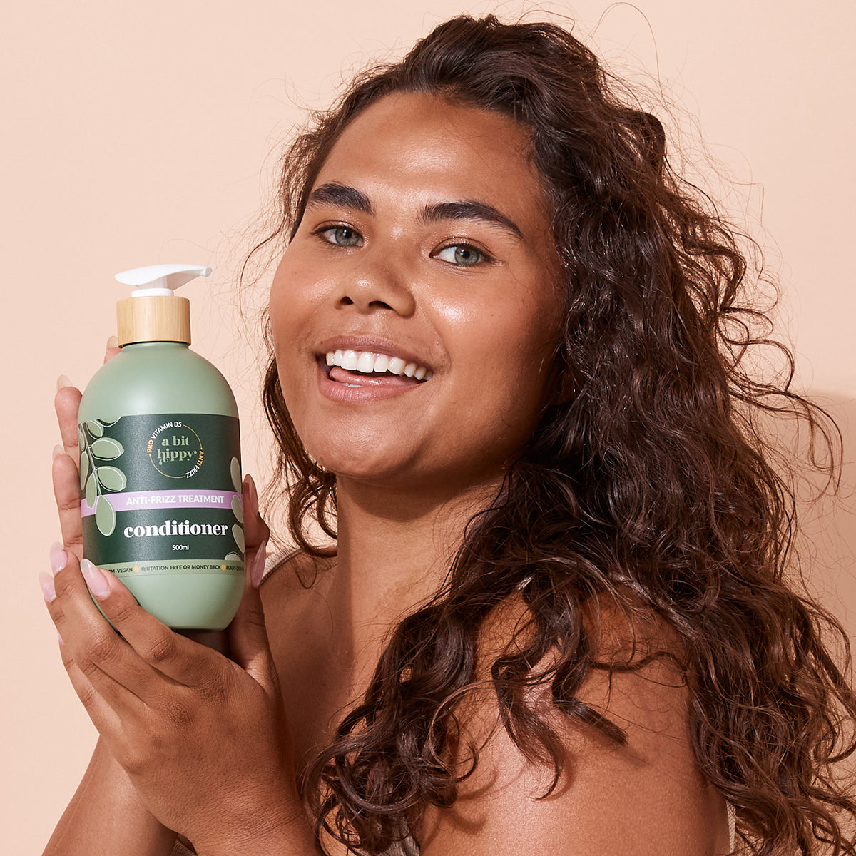 Smiling woman holding A bit Hippy Anti-Frizz Treatment Conditioner, natural haircare for smooth frizz-free curls