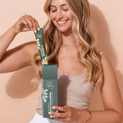 Smiling woman pulling a 50ml tube of Shampoo out of A bit Hippy Mini Essentials Pack, containing 50ml Shampoo, Conditioner, Body Lotion and cleanser. 