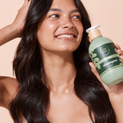 Woman holding A bit Hippy Sensitive Shampoo 500ml bottle on peach background, Silicones and SLS free hair care kit for healthy and shiny hair.