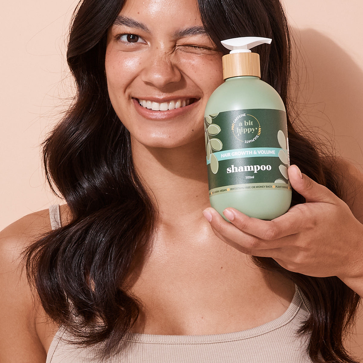 Woman holding A bit Hippy Hair Growth and Volume Shampoo 500ml bottle on peach background, anti sulphate formula with  Niacinamide and caffeine to boost hair growth.