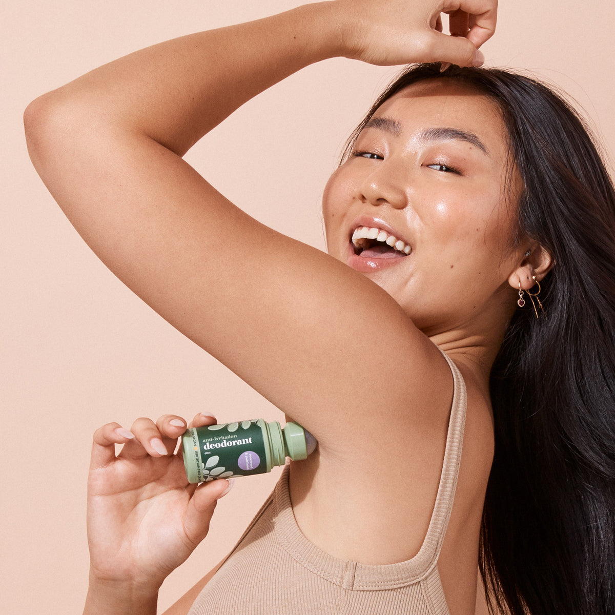 smiling woman applying bottle A bit Hippy Patchouli deodorant on peach background, aluminium free natural deodorant for sensitive skin.