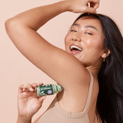 smiling woman applying bottle A bit Hippy Patchouli deodorant on peach background, aluminium free natural deodorant for sensitive skin.