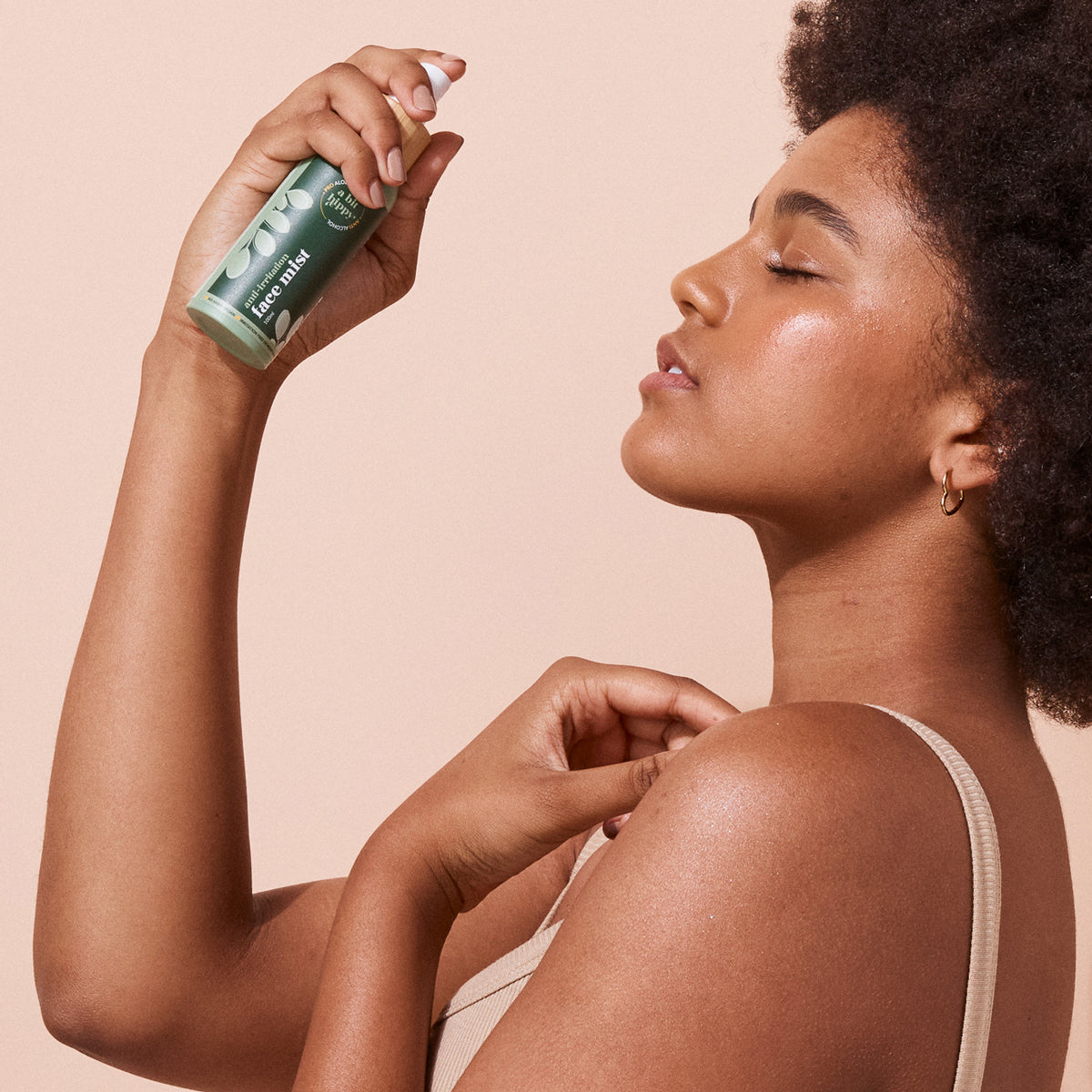 Woman applying A bit Hippy Face Mist onto face on peach background, refreshing face mist spray to prepare skin for moisturisers, sunscreen or makeup.
