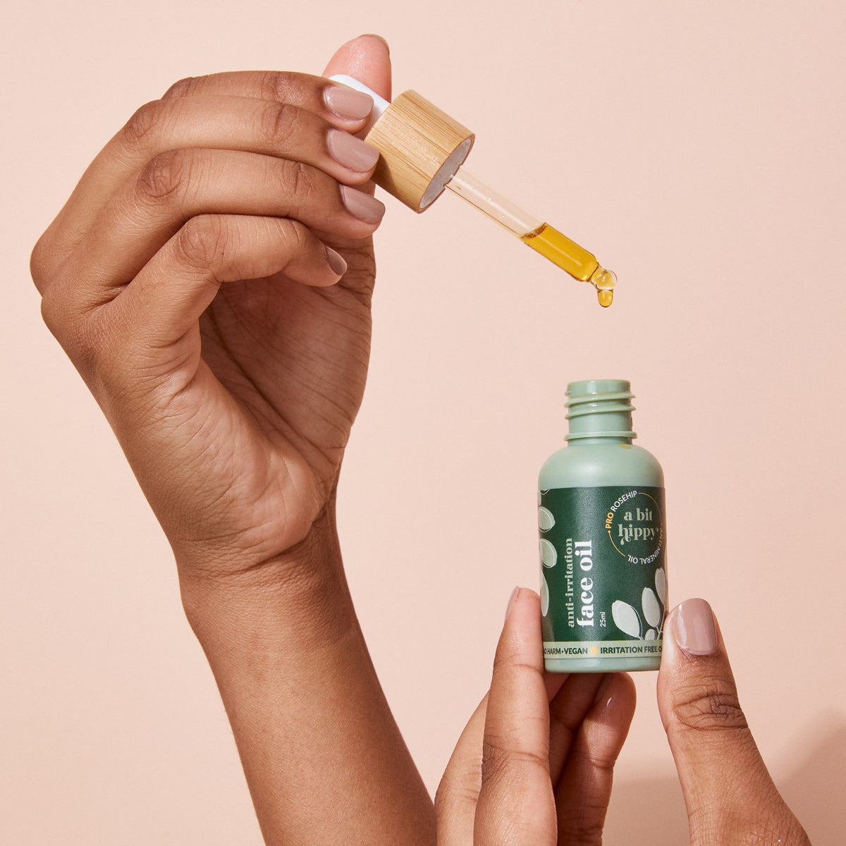 An open A bit Hippy Face Oil bottle on peach background, golden oil with Vitamin C and E along with Rosehip to improve skin elasticity and promote regeneration.