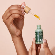 An open A bit Hippy Face Oil bottle on peach background, golden oil with Vitamin C and E along with Rosehip to improve skin elasticity and promote regeneration.