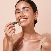 Smiling woman applying 5g tinted pomegranate A bit Hippy wind up lip balm on peach background, petroleum free natural lip balm. 