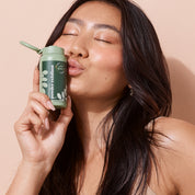 woman kissing bottle of A bit Hippy Powder Exfoliant on peach background, gentle exfoliant for sensitive skin.