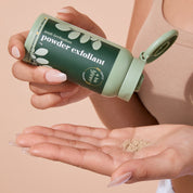 Woman applying A bit Hippy Powder Exfoliant onto hand on peach background, gentle exfoliant for sensitive skin.
